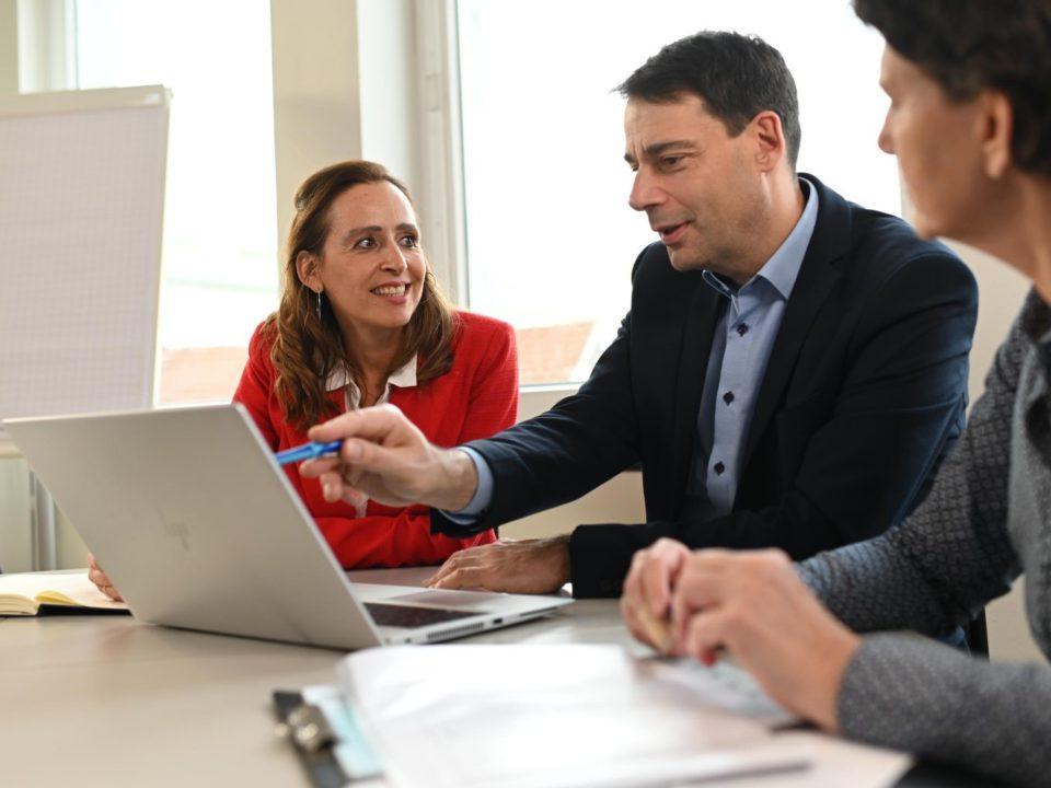 Two men looking at a laptop and talking with a woman